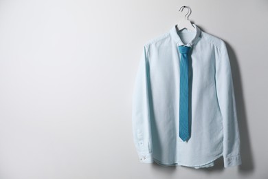 Photo of Hanger with shirt and necktie on light wall, space for text