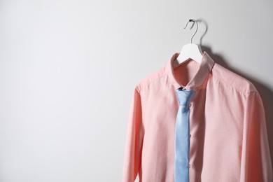 Photo of Hanger with shirt and necktie on light wall, space for text