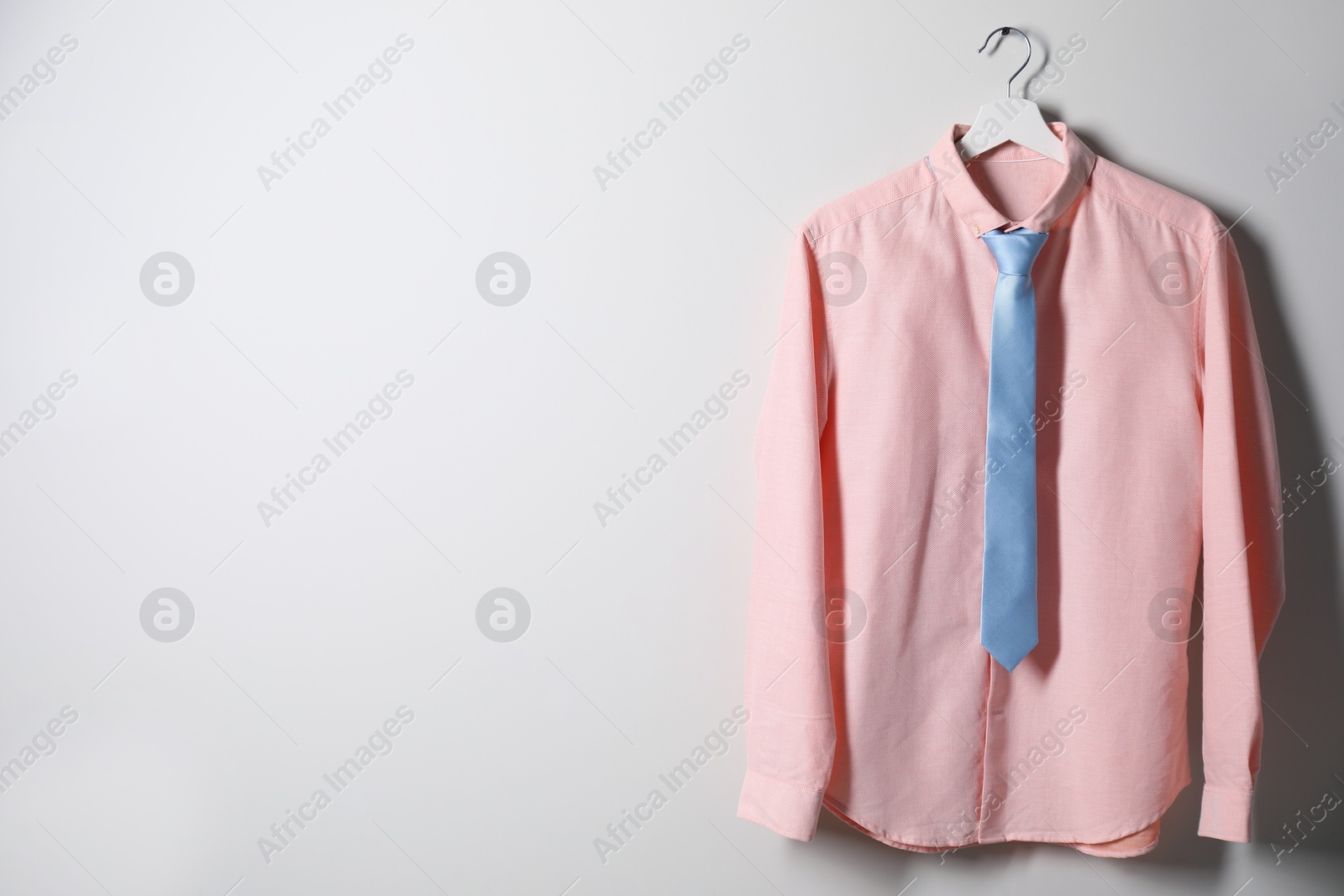 Photo of Hanger with shirt and necktie on light wall, space for text