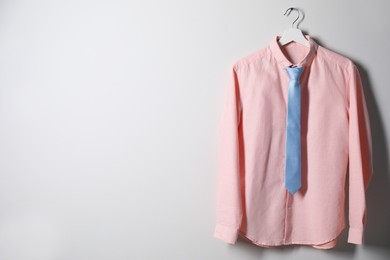 Photo of Hanger with shirt and necktie on light wall, space for text