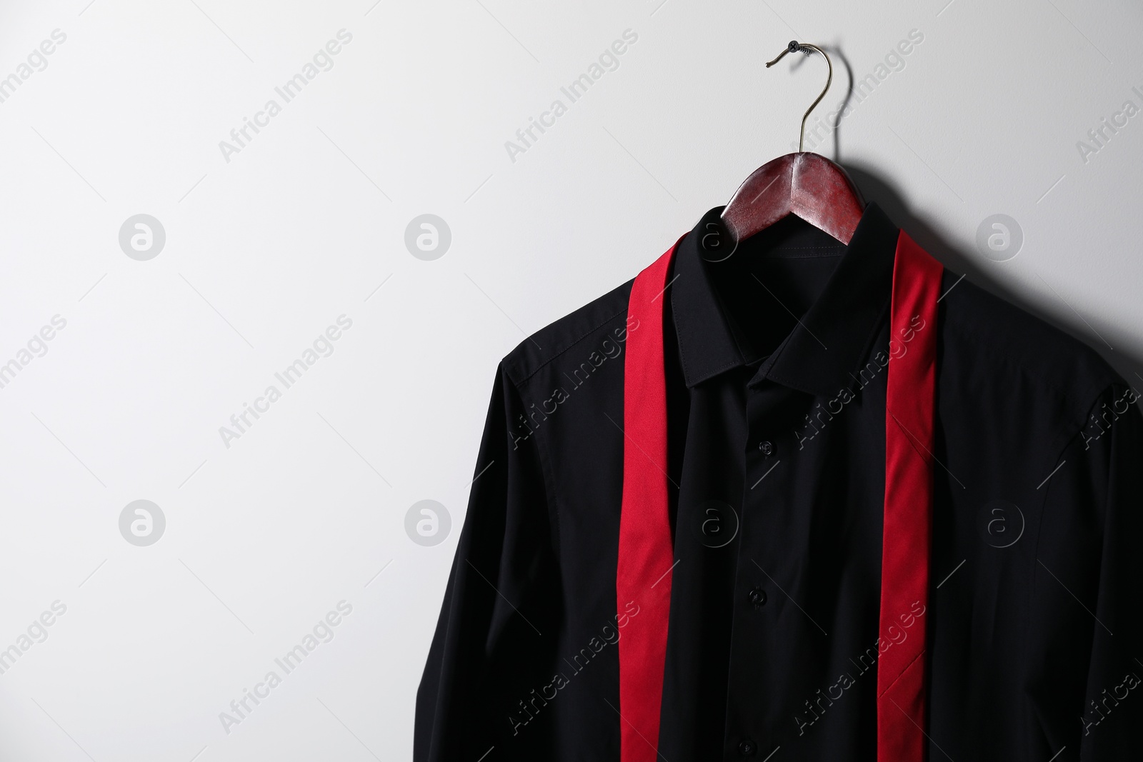 Photo of Hanger with black shirt and necktie on light wall, space for text