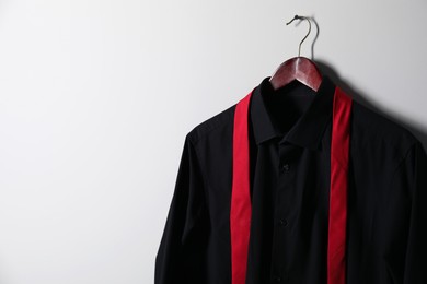 Hanger with black shirt and necktie on light wall, space for text