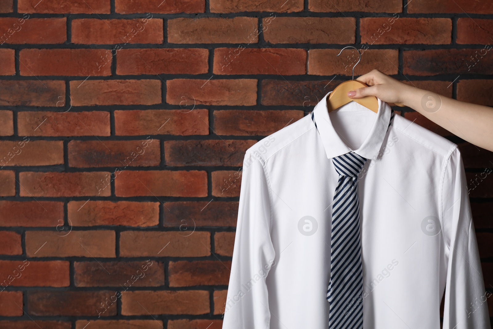 Photo of Woman holding hanger with shirt and necktie near red brick wall, space for text