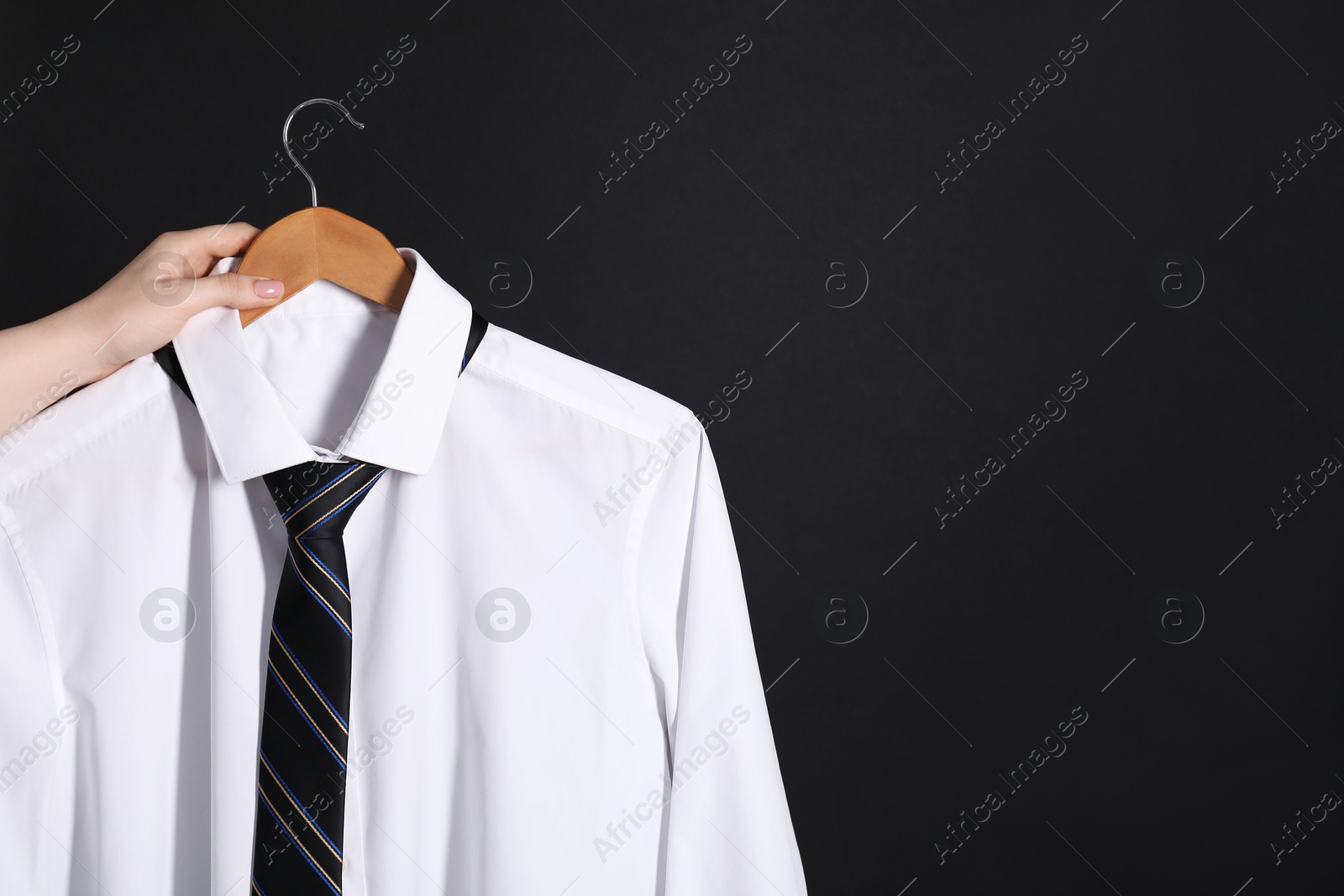 Photo of Woman holding hanger with white shirt and necktie on black background, space for text