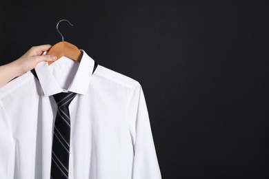 Woman holding hanger with white shirt and necktie on black background, space for text