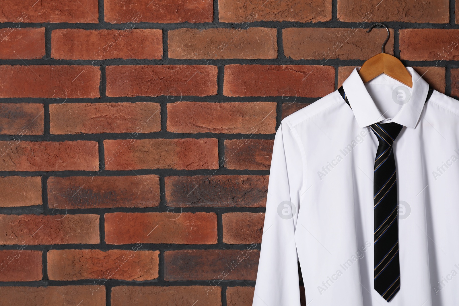 Photo of Hanger with white shirt and striped necktie on red brick wall, space for text