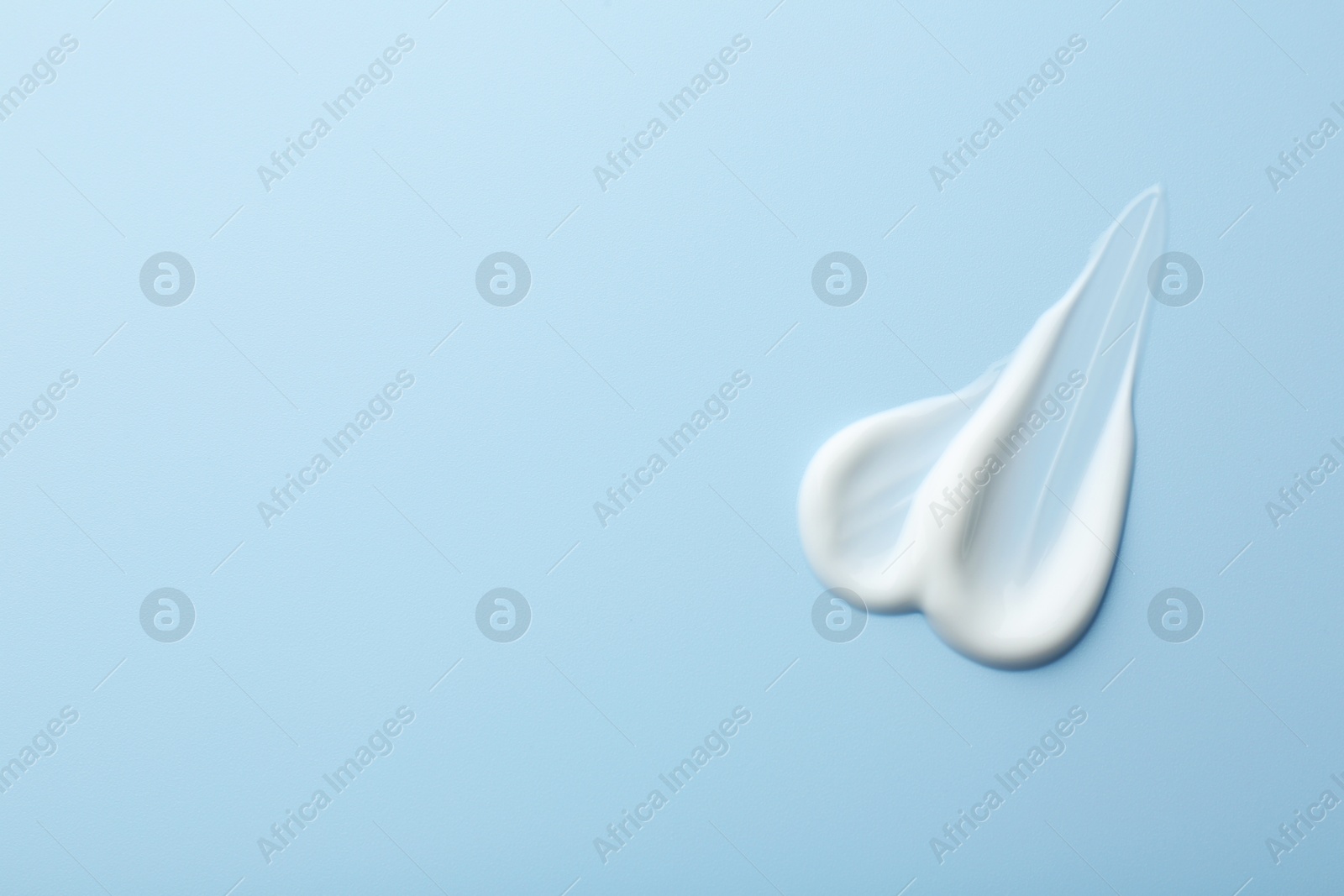 Photo of Sample of face cream on light blue background, top view. Space for text