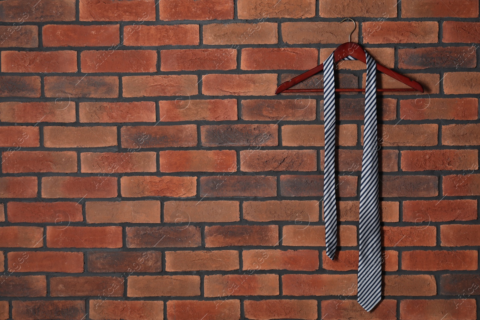 Photo of Hanger with striped necktie on red brick wall. Space for text