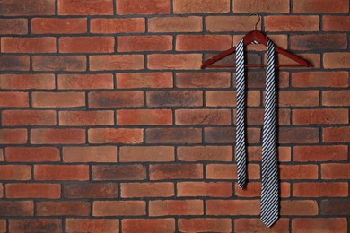 Photo of Hanger with striped necktie on red brick wall. Space for text