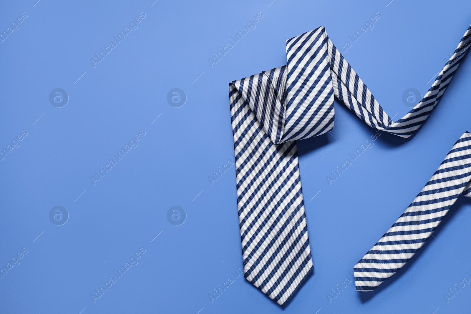 Photo of Stylish striped necktie on blue background, top view. Space for text