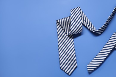 Stylish striped necktie on blue background, top view. Space for text