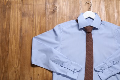 Hanger with light blue shirt and stylish necktie on wooden background, top view. Space for text