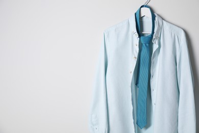 Hanger with stylish shirt and turquoise necktie on light wall, space for text