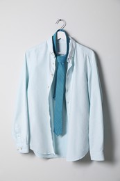 Hanger with stylish shirt and turquoise necktie on light wall