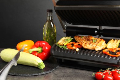 Photo of Electric grill with different products and knife on grey textured table