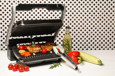 Photo of Electric grill with different products and tongs on white table