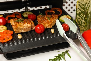 Electric grill with different products and tongs on white table