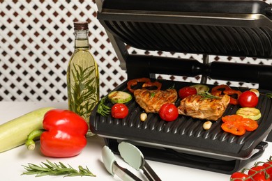 Electric grill with different products and tongs on white table