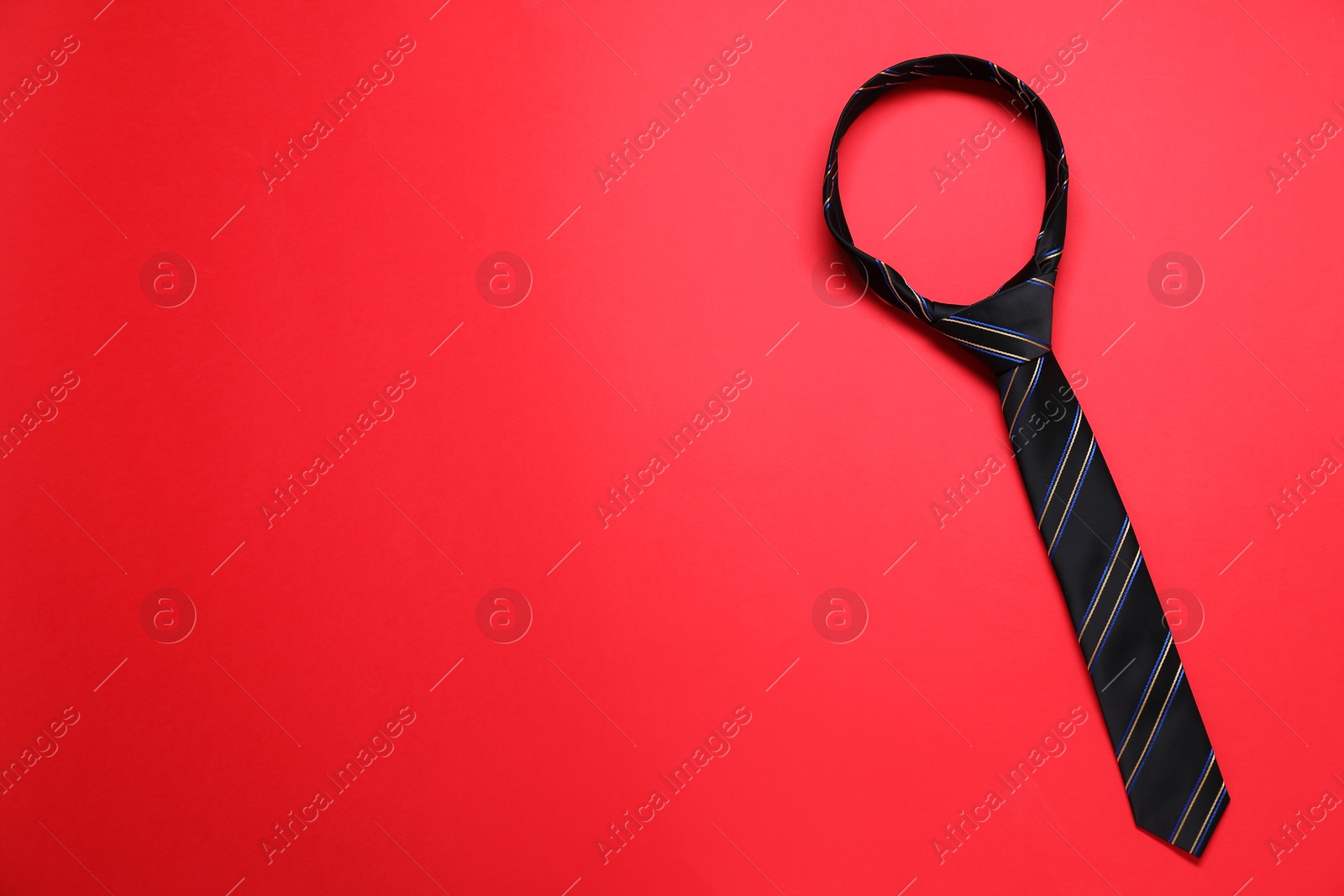 Photo of Striped necktie on red background, top view. Space for text
