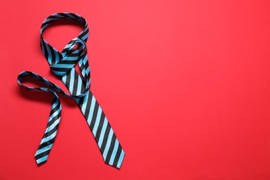 Photo of Striped necktie on red background, top view. Space for text