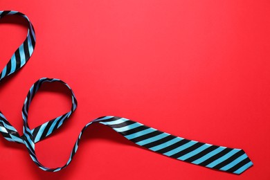 Striped necktie on red background, top view. Space for text