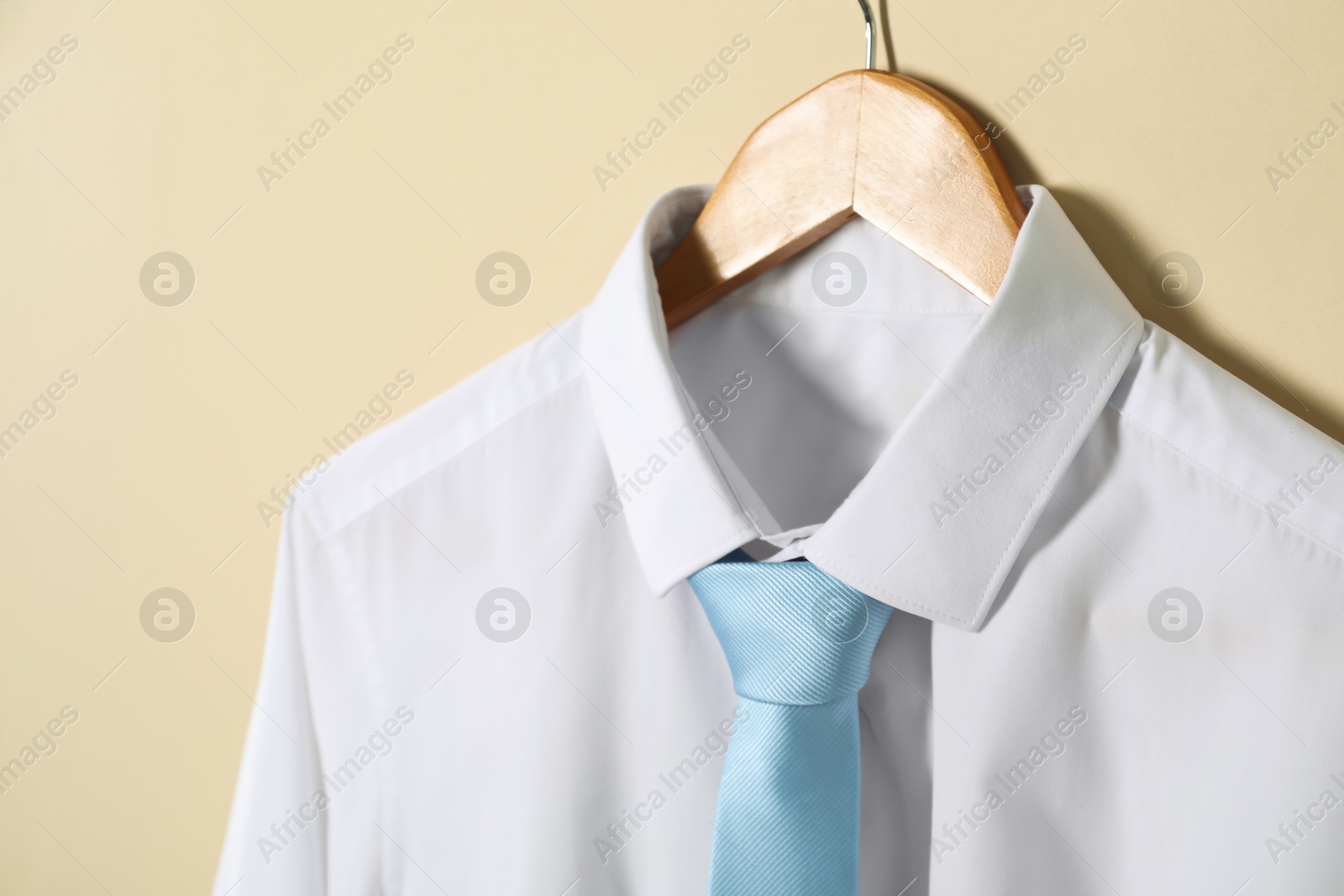 Photo of Hanger with shirt and necktie on beige background
