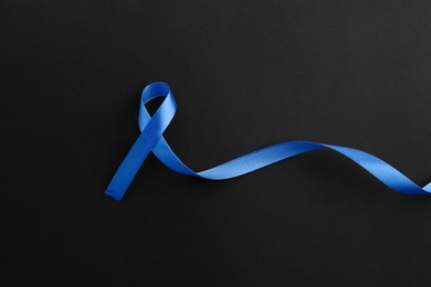 Photo of Blue awareness ribbon on black background, top view