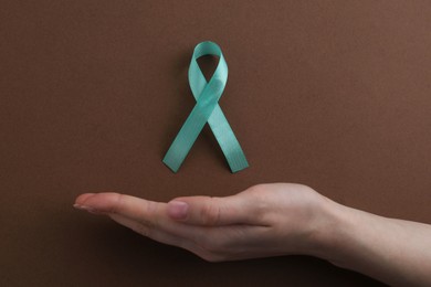 Photo of Woman with turquoise awareness ribbon on brown background, top view