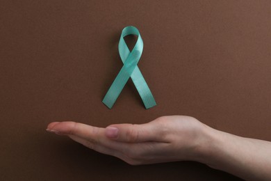 Woman with turquoise awareness ribbon on brown background, top view