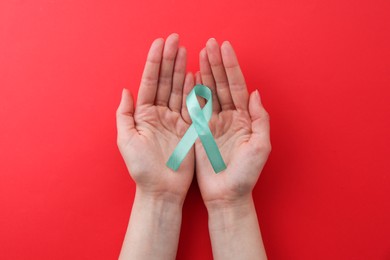 Woman holding turquoise awareness ribbon on red background, top view