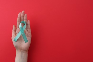 Woman holding turquoise awareness ribbon on red background, top view. Space for text