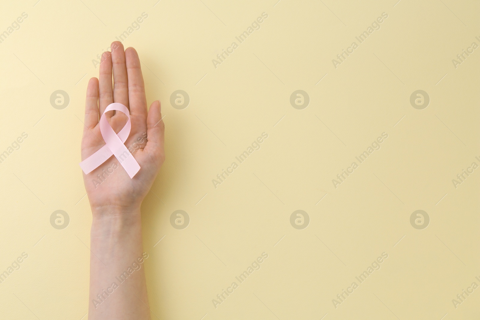 Photo of Woman with pink awareness ribbon on pale yellow background, top view. Space for text