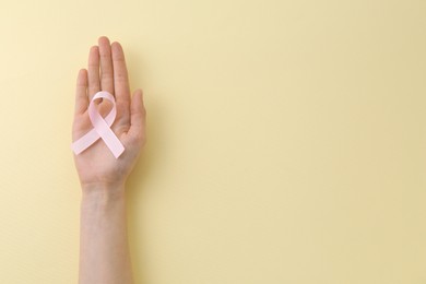 Woman with pink awareness ribbon on pale yellow background, top view. Space for text