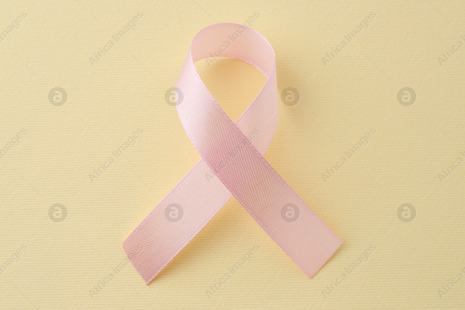 Photo of Pink awareness ribbon on pale yellow background, top view