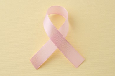 Pink awareness ribbon on pale yellow background, top view