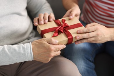 Photo of Son giving gift box to his dad on sofa, closeup