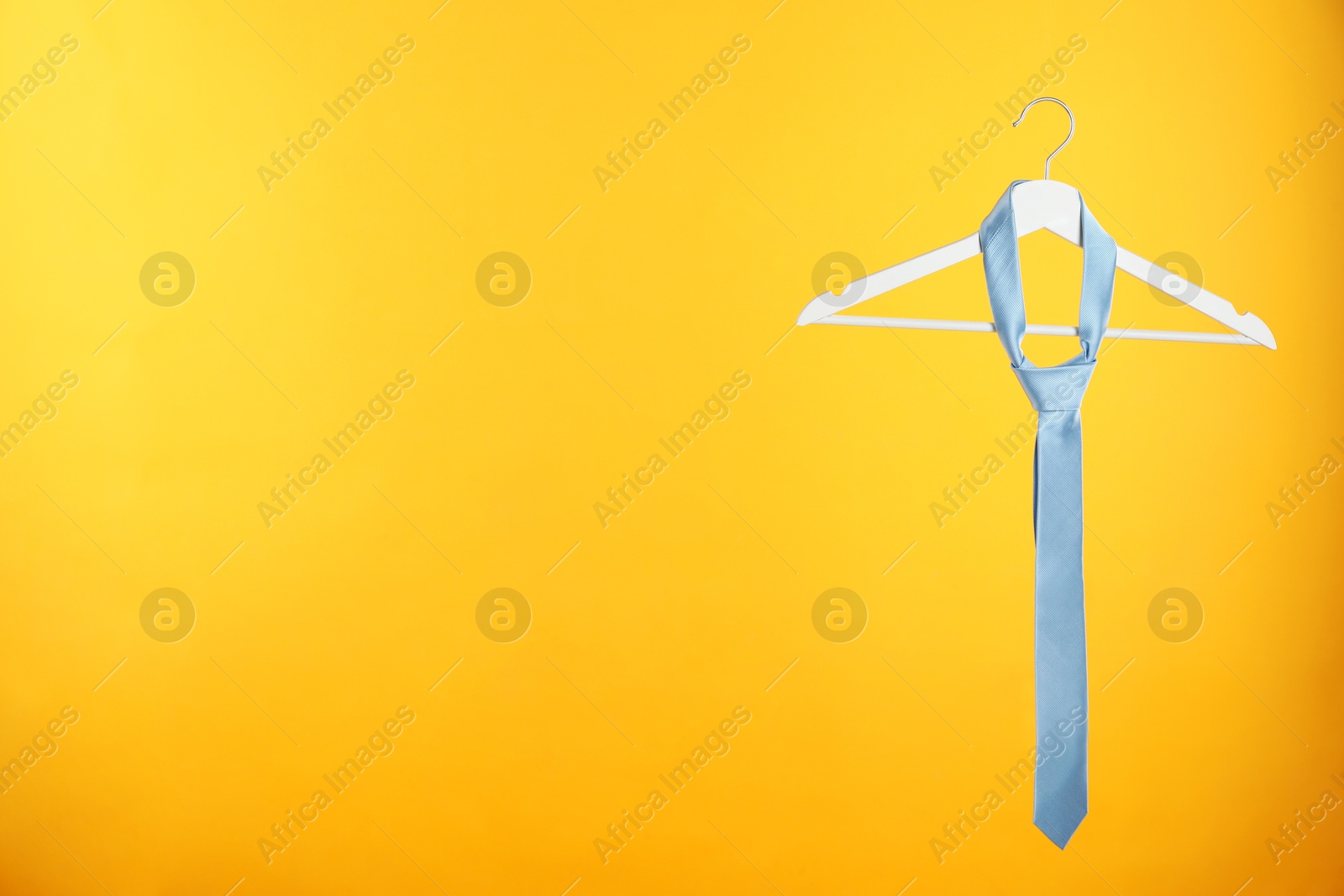 Photo of Hanger with light blue tie against orange background. Space for text