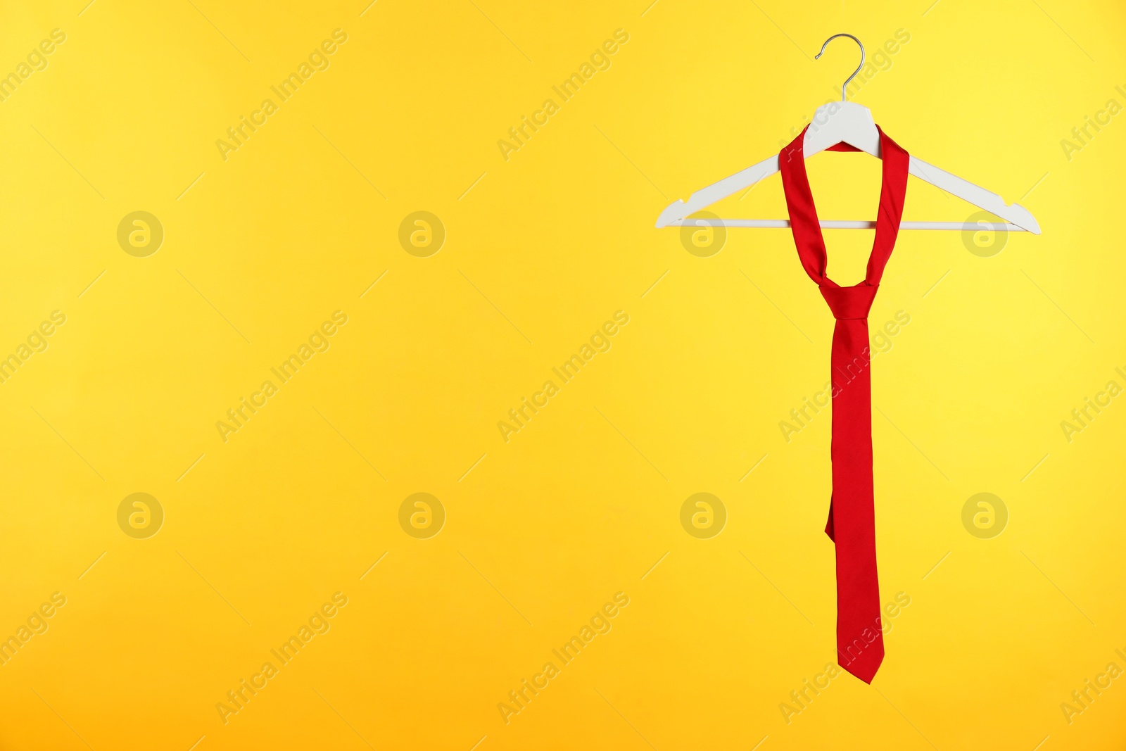 Photo of Hanger with red tie against orange background. Space for text