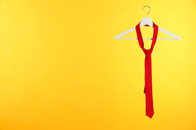 Photo of Hanger with red tie against orange background. Space for text