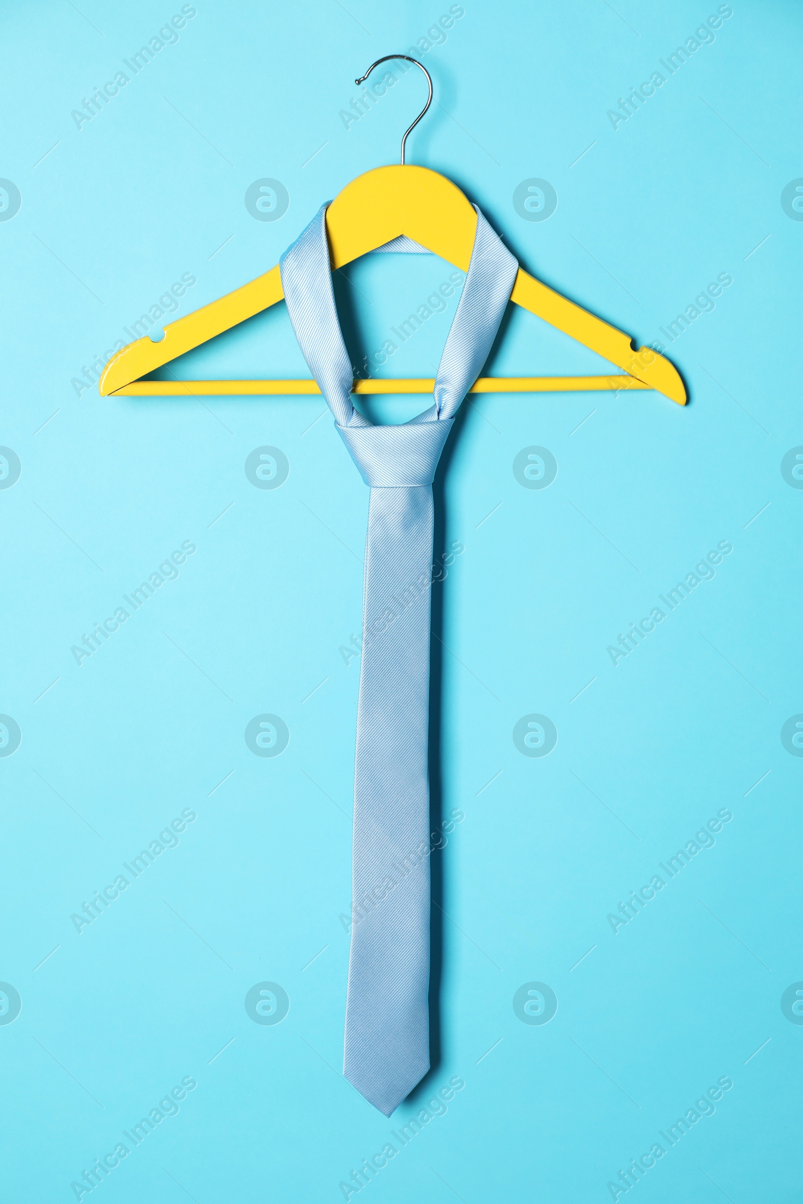 Photo of Hanger with silk tie on light blue background