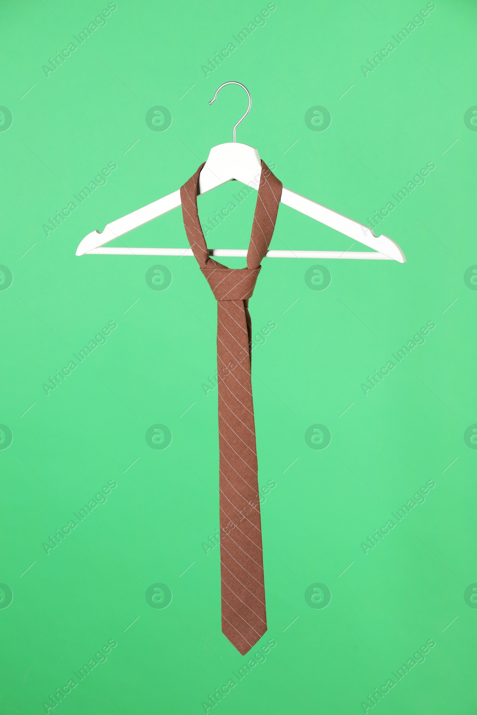 Photo of Hanger with brown striped tie on green background