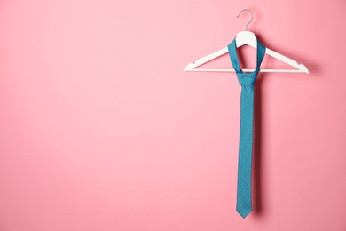 Photo of Hanger with turquoise tie on pink background. Space for text
