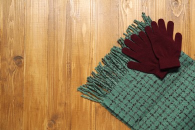 Soft green scarf and gloves on wooden table, top view. Space for text