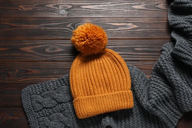 Knitted scarf and hat on wooden table, top view. Space for text