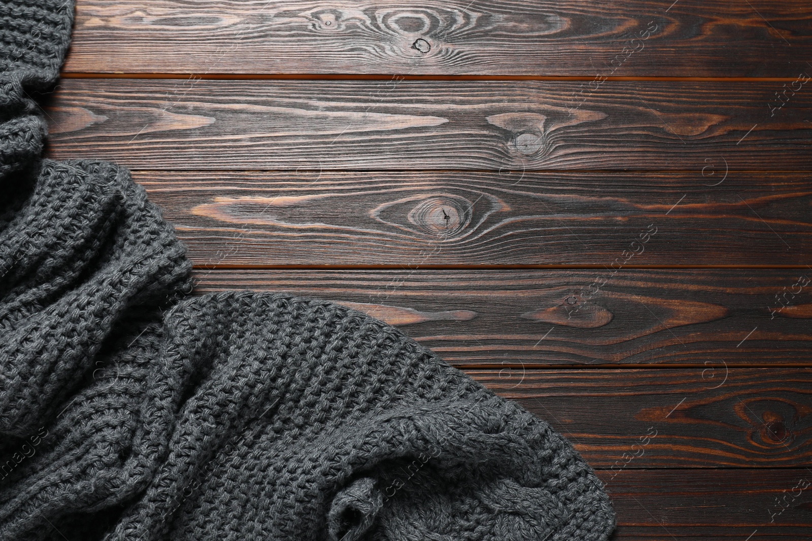 Photo of Gray knitted scarf on wooden table, top view. Space for text