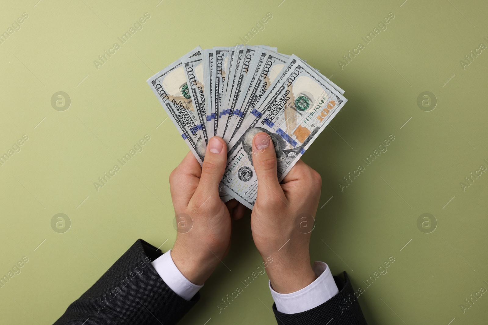 Photo of Money exchange. Man holding dollar banknotes on olive background, top view