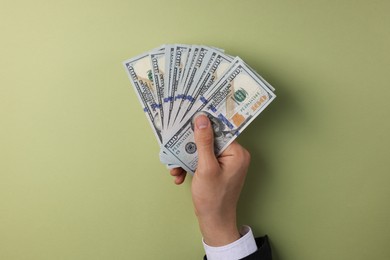 Photo of Money exchange. Man holding dollar banknotes on olive background, top view