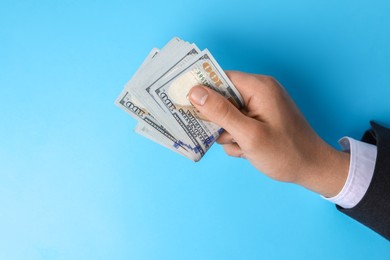 Photo of Money exchange. Man holding dollar banknotes on light blue background, top view