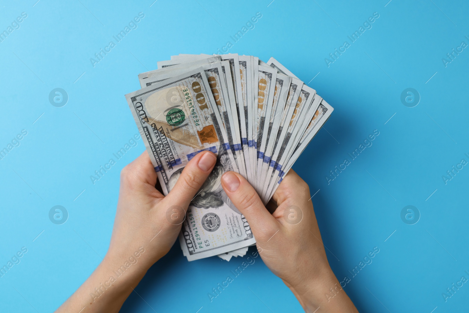 Photo of Money exchange. Woman holding dollar banknotes on light blue background, top view