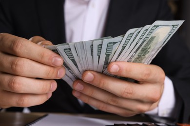 Photo of Money exchange. Man counting dollar banknotes at table, closeup